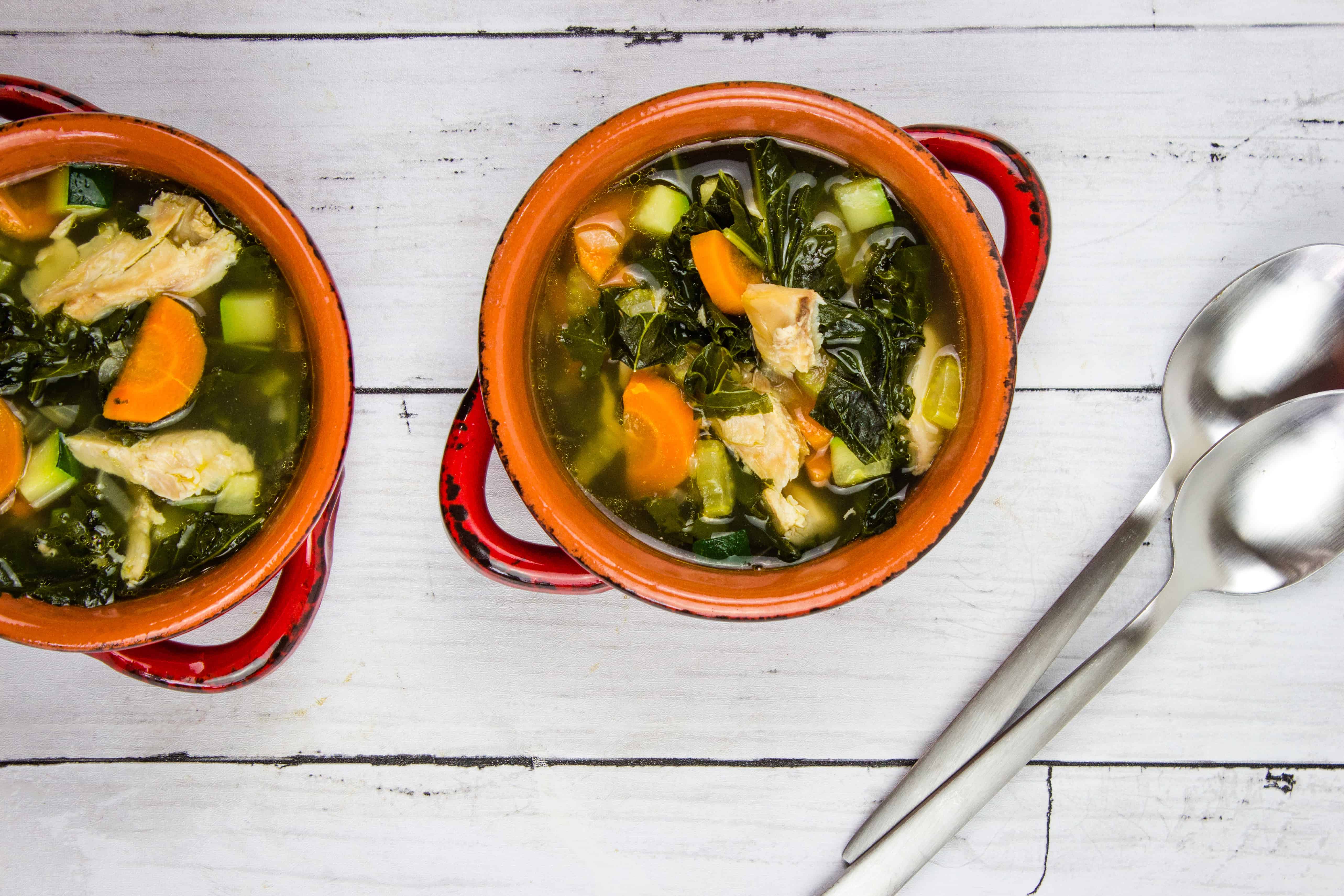 Two bowls of turkey and vegetable soup with spoons.