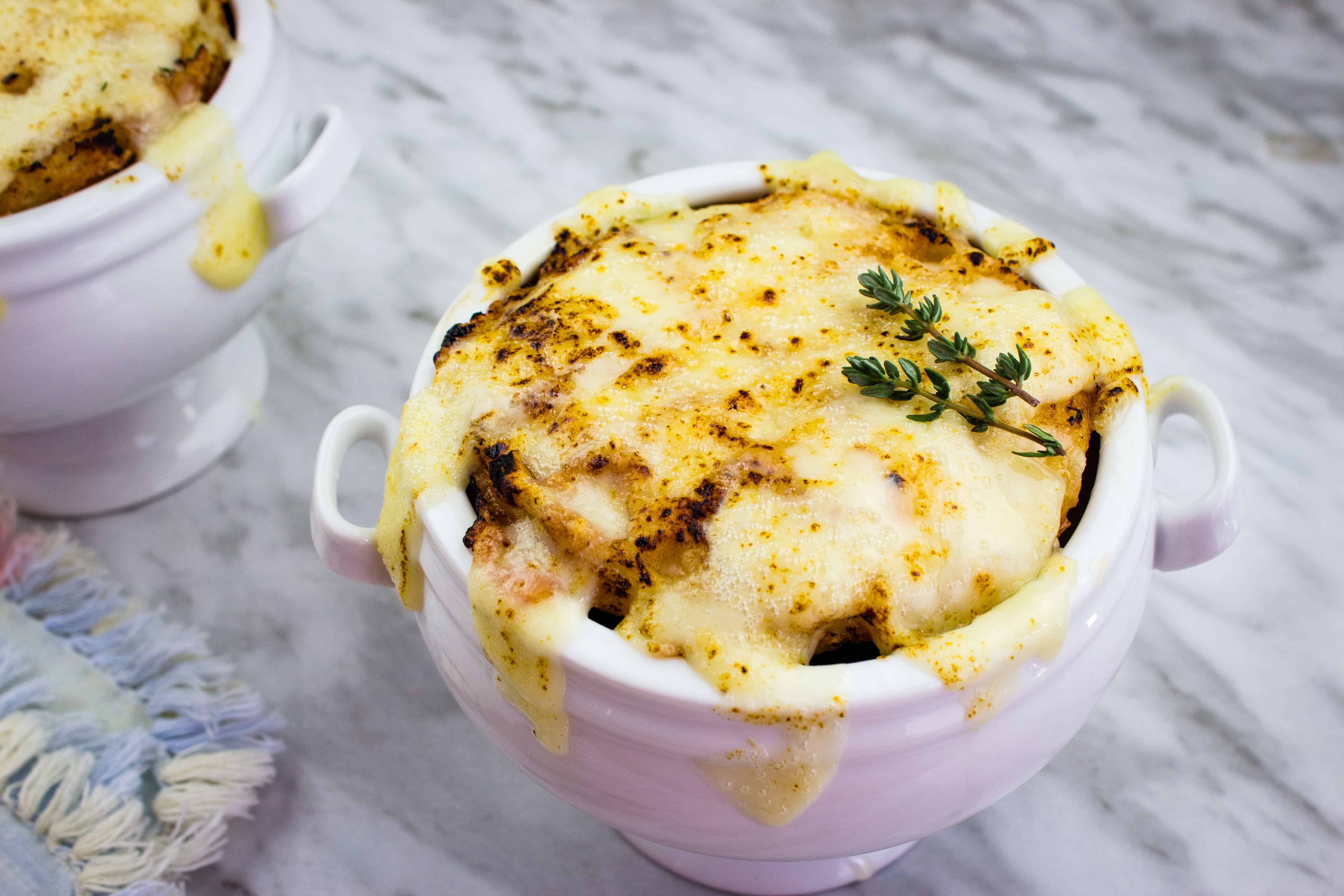 Low-Carb French Onion Soup in a tall white bowl on a marble counter.